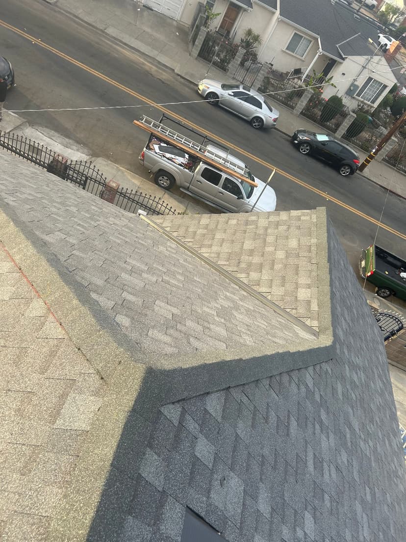 Aerial view of a residential roof showing shingle pattern and nearby parked vehicles.