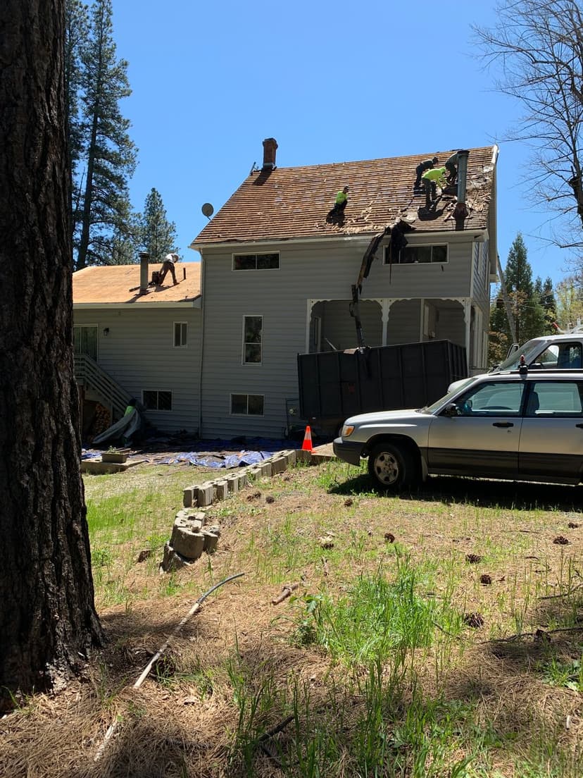 Roofing contractors working on a house; blue sky and trees in the background.
